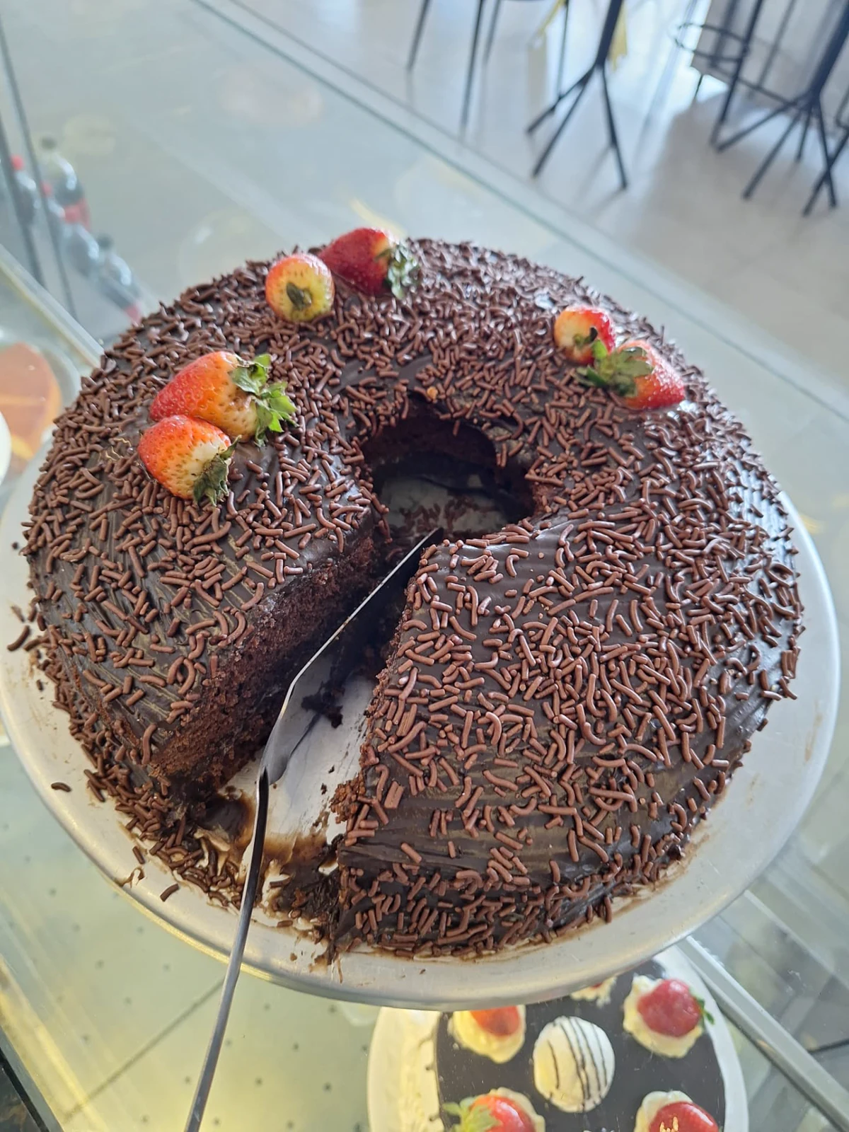 Bolo de chocolate da ManáPan coberto com granulado e morangos, com fatia retirada mostrando a massa fofa
