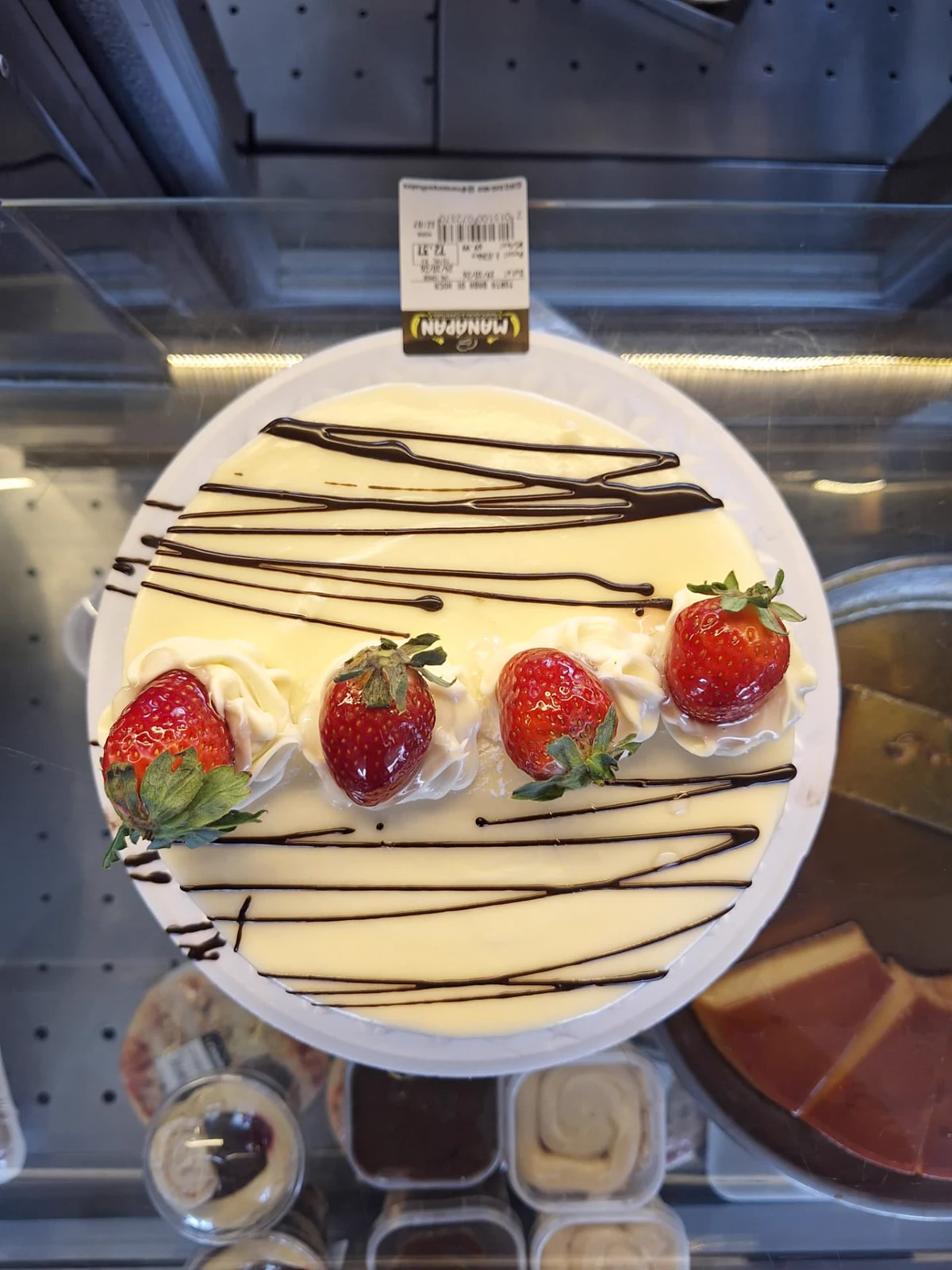 Torta de creme branco da ManáPan decorada com morangos frescos e fios de chocolate, vista de cima na vitrine