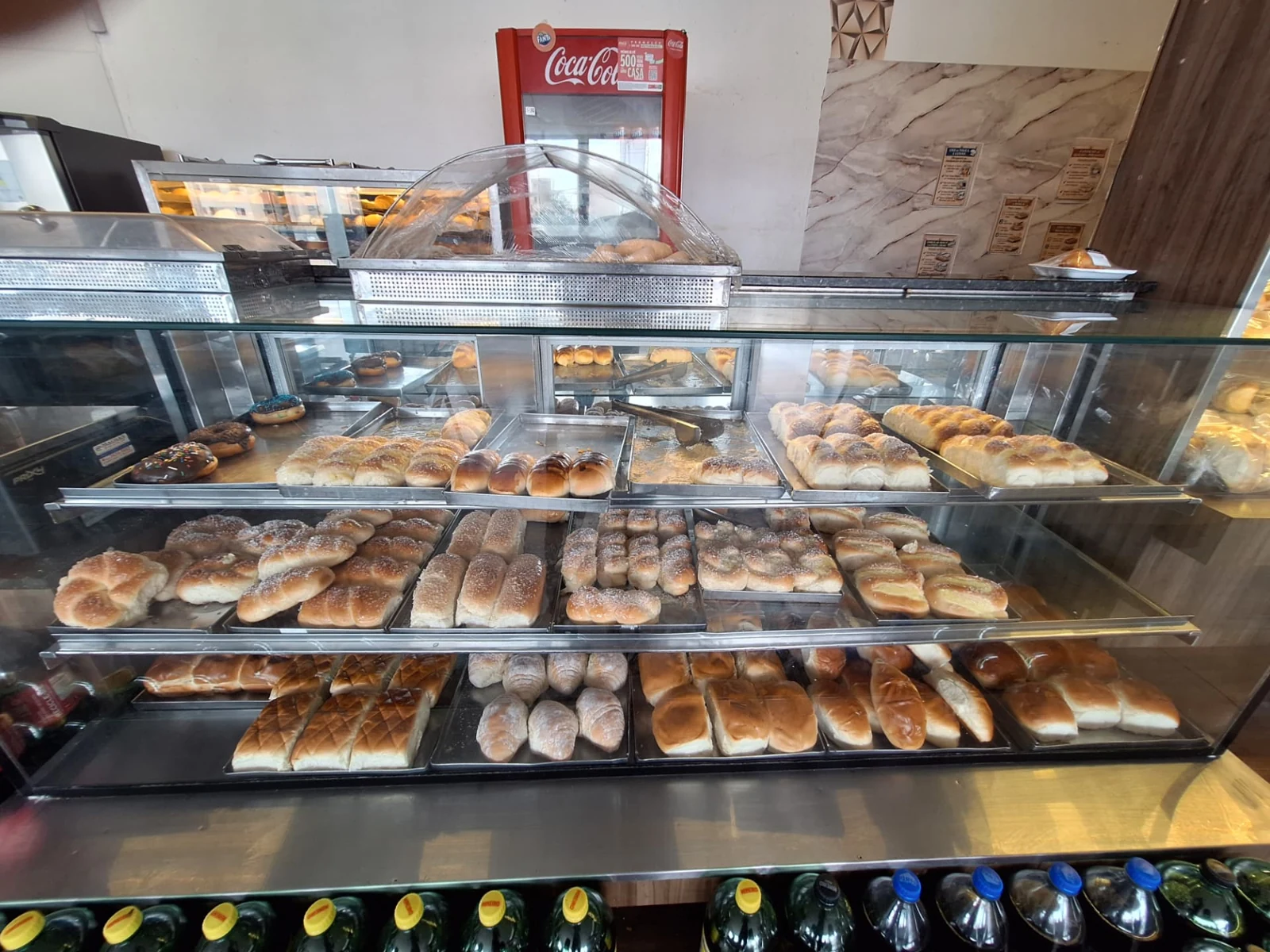 Vitrine de vidro da ManáPan com bandejas de pães doces, roscas e pães cobertos com açúcar